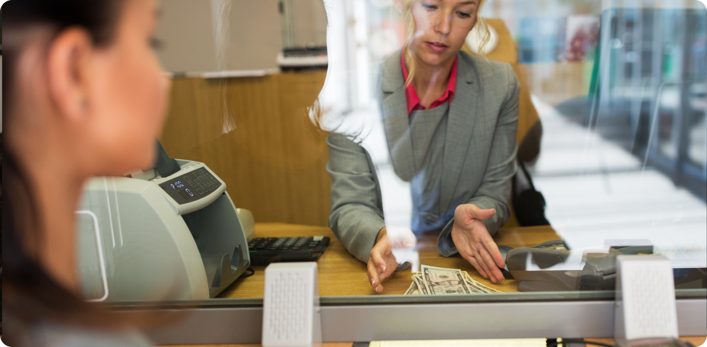Bank teller counting money behind glass, highlighting urgency of improving branch talent retention in banking