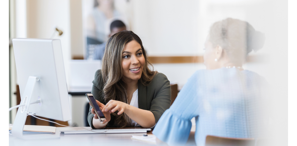 Smiling professional shows a customer her phone at a service desk, building customer trust through confident communication.